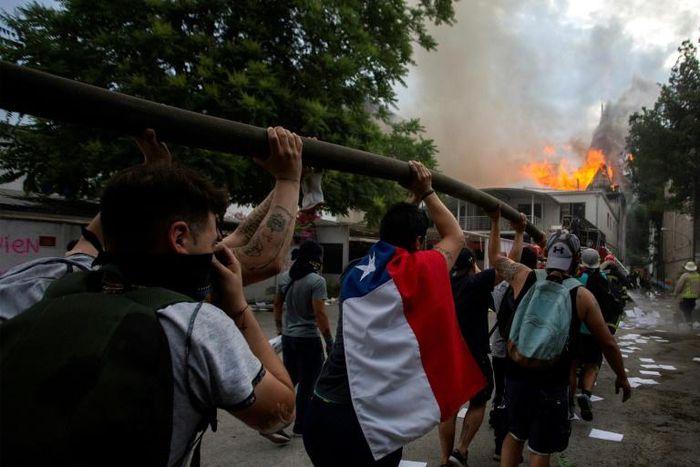 Demonstrators hold up a hose as flames engulf the Pedro de Valdivia University following a protest against the government of Chilean President Sebastian Pinera in Santiago, on November 8, 2019.Unrest began in Chile last October 18 with protests against...