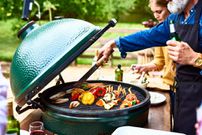 Man using tongues to turn vegetables on bbq
