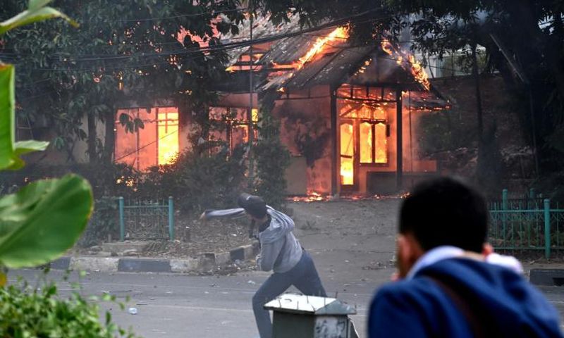 A building goes up in flames in Jakarta as a protester hurls rocks at police during violent demonstrations against the government's proposed change to the criminal code
