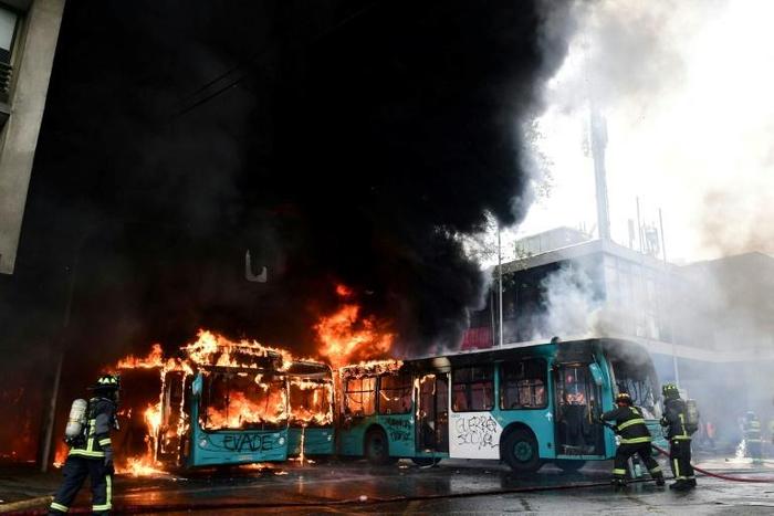 Chilean firefighters extinguish burning buses during clashes between protesters and the riot police in Santiago, on October 19, 2019.Chile's president declared a state of emergency in Santiago Friday night and gave the military responsibility for secur...