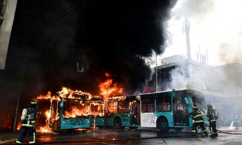 Chilean firefighters extinguish burning buses during clashes between protesters and the riot police in Santiago, on October 19, 2019.Chile's president declared a state of emergency in Santiago Friday night and gave the military responsibility for secur...