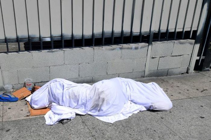 A homeless person' sleeping under a sheet on a sidewalk in Los Angeles, California on August 22, 2019, home to one of the nation's largest homeless populations