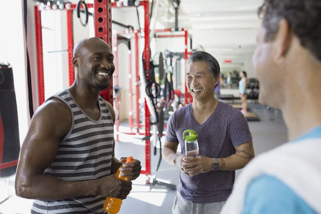 Smiling men with water bottles talking at gym