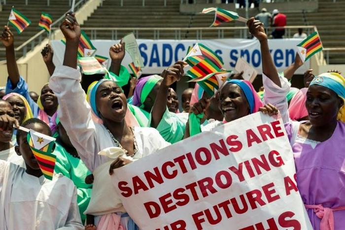Demonstrators chant slogans and wave Zimbabwe's national flag during a rally to denounce US and EU economic sanctions