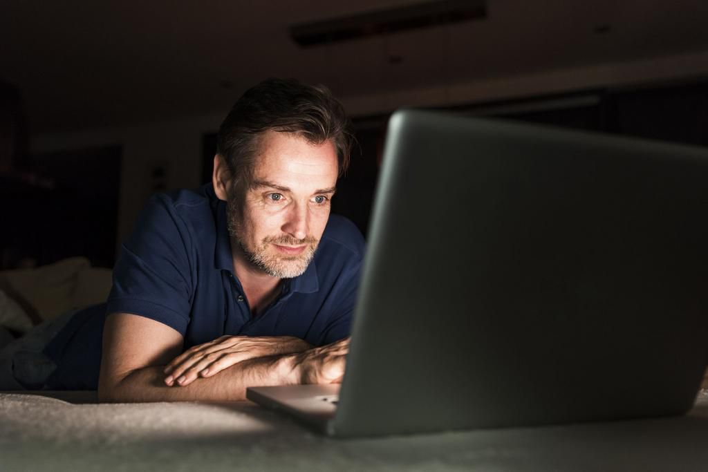 Portrait of man lying on couch at home looking at laptop