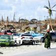A woman walks by destroyed cars in The Mudd neighborhood of Marsh Harbour