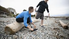 Young male amputee tying shoe on beach, talking with boyfriend