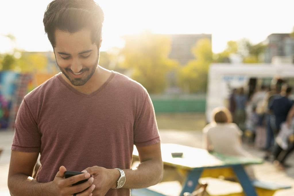 Young man texting with smart phone in sunny park