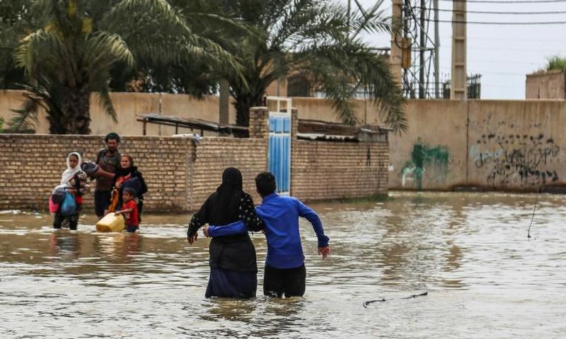 An Iranian family walks through a flooded street in a village around the city of Ahvaz