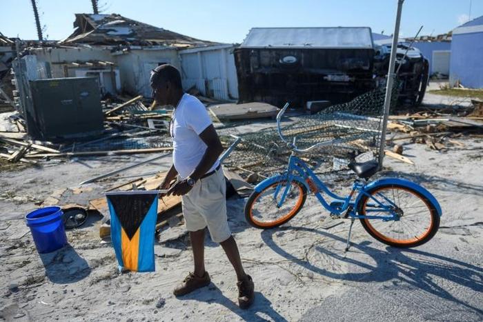 Irvin Russell carries the Bahamian flag as he walks past a damaged truck on Treasure Cay in the hurricane-hit Bahamas