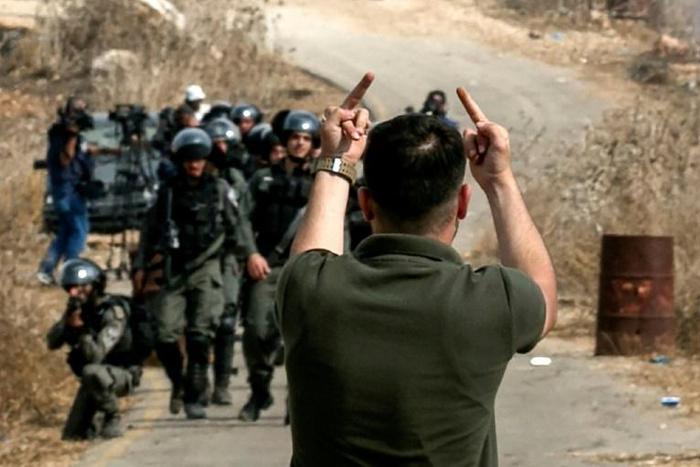 A Palestinian protester makes an insulting gesture to Israeli border guards during a protest against construction of an Israeli outpost near an Israeli settlement in the occupied West Bank