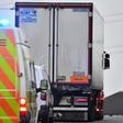 Police drive away a lorry, with black plastic visible at the rear, in which 39 dead bodies were discovered, sparking a murder investigation