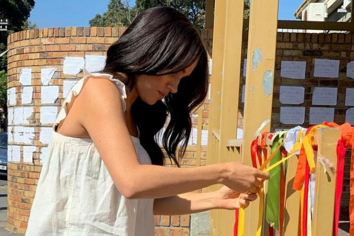 The Duchess of Sussex ties on a ribbon as she visits the memorial to murdered South African student Uyinene Mrwetyana in Cape Town in solidarity with victims of gender violence