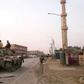 Members of the pro-Syrian government forces ride on a tank as it drives down a street in the Syrian border town of Albu Kamal