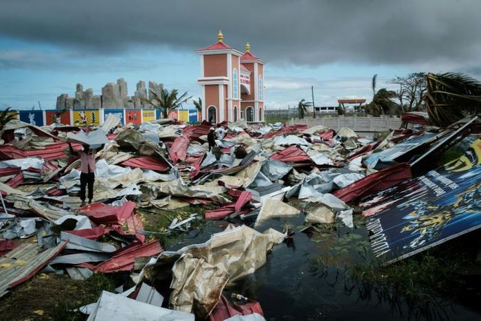 People collect metal sheets from a damaged supermarket to rebuild their houses destroyed by Cyclone Idai in Beira, Mozambique