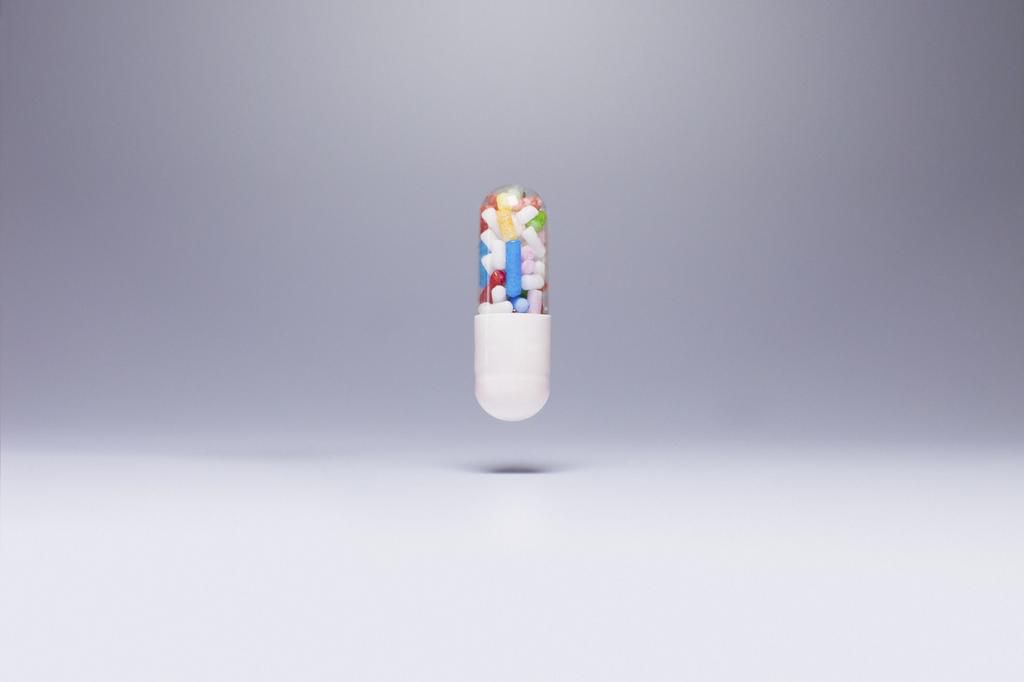Capsule containing sprinkles in mid-air against gray background