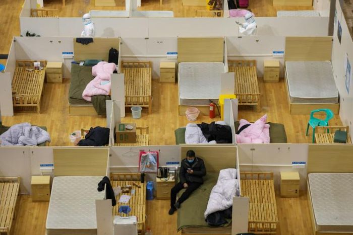 Medical workers (top) walk past empty beds at a makeshift hospital in a stadium in Wuhan. A top official hinted that the quarantine of Hubei could soon be lifted
