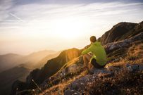 Italy, mountain running man sitting on rock looking at sunset