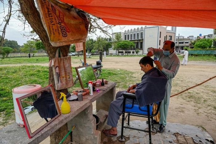 A barber wearing a facemask cuts a customer's hair at an open-air stall in Islamabad