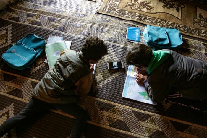 Young pupils follow a lesson on a mobile telephone at a camp for displaced Syrians in the village of Kafr Yahmoul in northwestern Idlib province