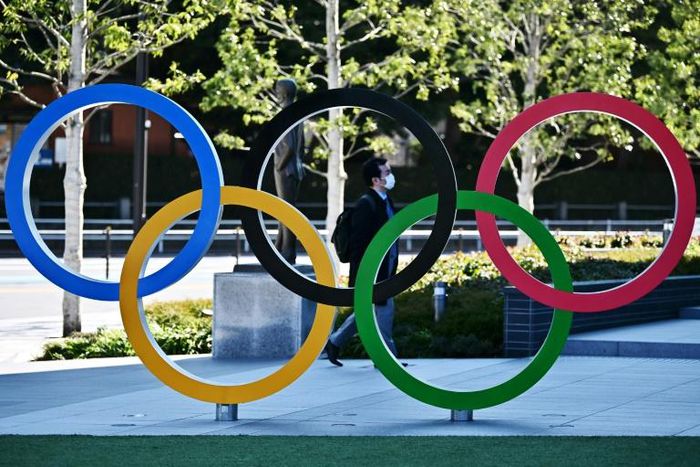 A man wearing a face mask (background C) walks past an installation of the Olympic rings in Tokyo on February 28, 2020.The International Olympic Committee is "committed" to holding the 2020 Games in Tokyo as planned despite the widening new coronavirus...