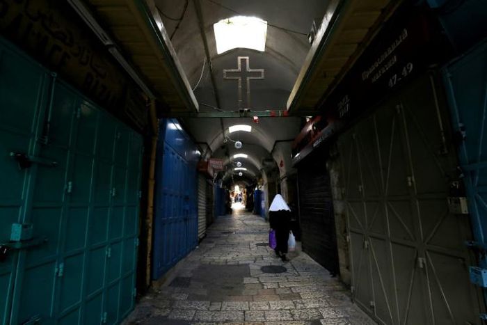 A woman walks past closed shops along a deserted alley in the Old City of Jerusalem