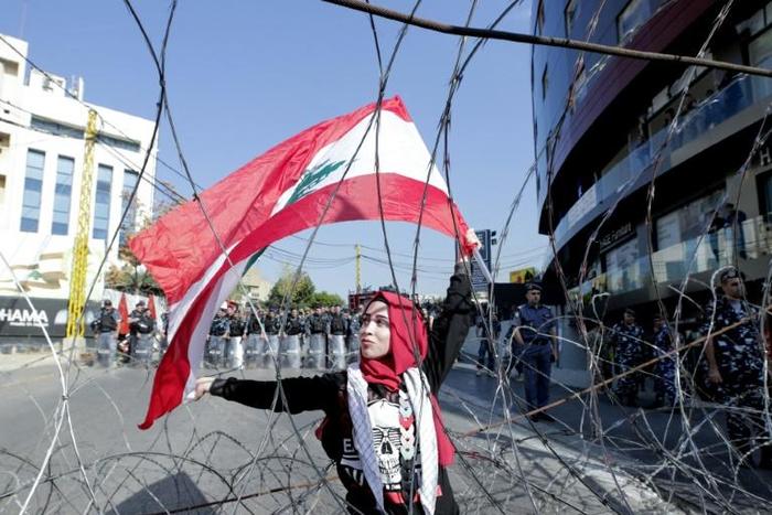 A Lebanese demonstrator waves the national flag while security forces stand by