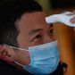 A hotel employee takes the temperature of a man who just arrived in the building in Wuhan
