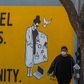 A man wearing gloves and a face mask walks by a mural reading "Cancel Plans Not Humanity" in Los Angeles, California