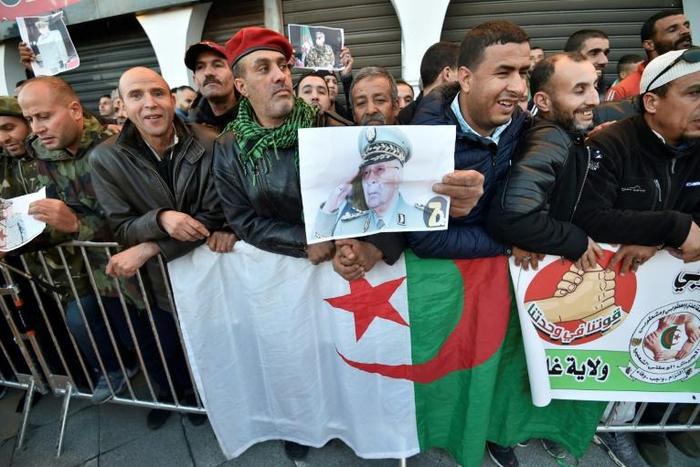 People stand with national flags and portraits of Gaid Salah as they gather outside the People's Palace during his funeral in Algiers