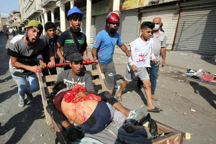 Iraqi demonstrators evacuate a man wounded in clashes with security forces on Baghdad's Martyrs' Bridge (Jisr Al-Shuhada)