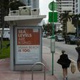 People walk past a billboard in Miami Beach discussing sea level rise: dozens of trucks have started dumping hundreds of thousands of tons of sand on Miami Beach as part of US government measures to protect Florida's tourist destinations against the ef...