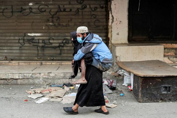 A woman carries a disabled man wearing a protective face mask in the Sabra refugee camp in Lebanon where vulnerable Syrian and Palestinian refugees are bracing for the coronavirus