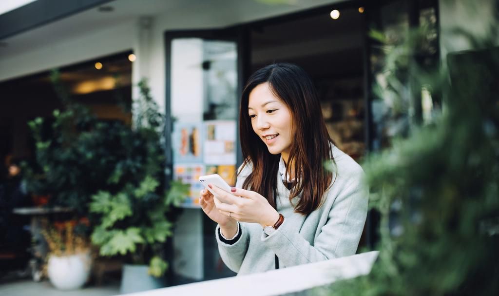 Beautiful Asian lady using smartphone and relaxing in outdoor cafe