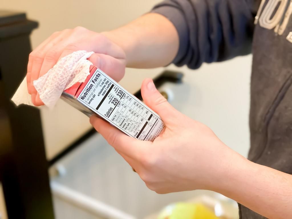 father uses anti-bacterial wipe to sanitize groceries delivered by a grocery delivery service