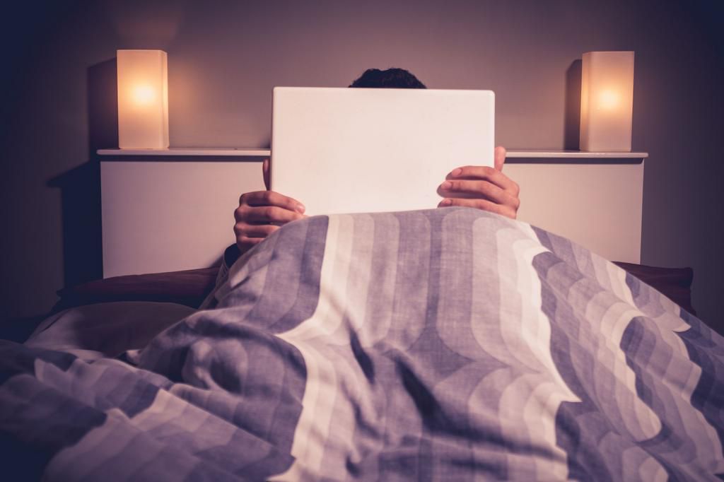 Man is sitting in bed behind his laptop