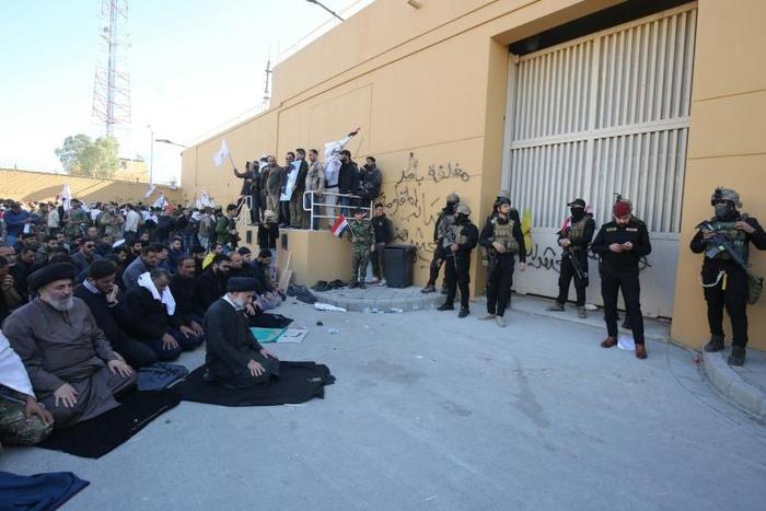 Iraqi security forces stand guard as protesters hold a prayer inside the walls of the US embassy in Baghdad's Green Zone