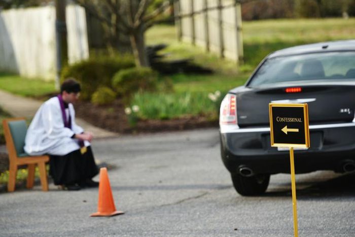 Father Scott Holmer is careful to keep a safe distance from his flock and asks parishioners to stay in their vehicles