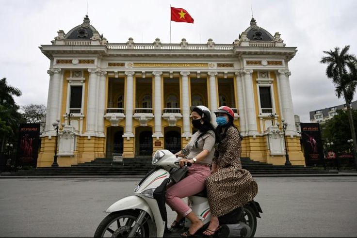 Women wearing face masks ride past the Opera House in Hanoi on April 23, 2020, as Vietnam eased its nationwide social isolation effort to prevent the spread of the COVID-19 novel coronavirus. Vietnam eased social distancing measures on April 23, with e...