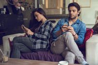 Young couple text messaging on cell phones and ignoring each other.