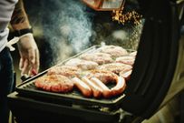 Man seasoning burgers and hot dogs on barbecue