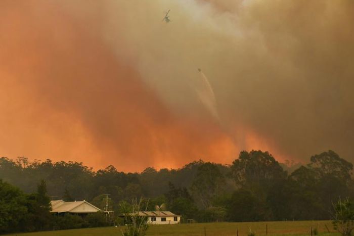 A helicopter drops water on a homestead as bushfires rage north of Sydney