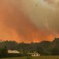 A helicopter drops water on a homestead as bushfires rage north of Sydney