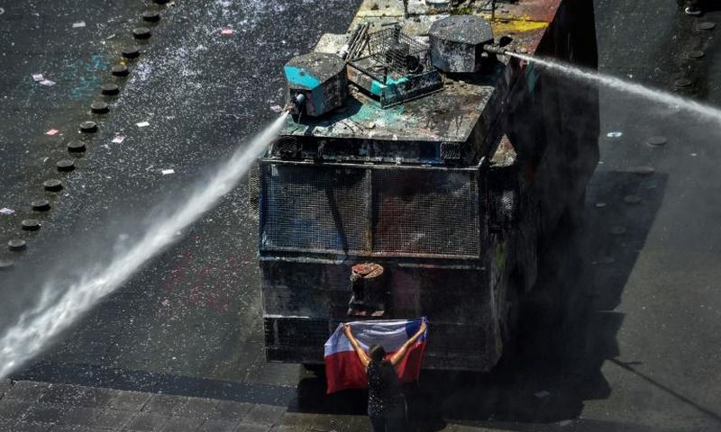 A demonstrator stands in front of police water cannon in Santiago, Chile, which has been rocked by protests