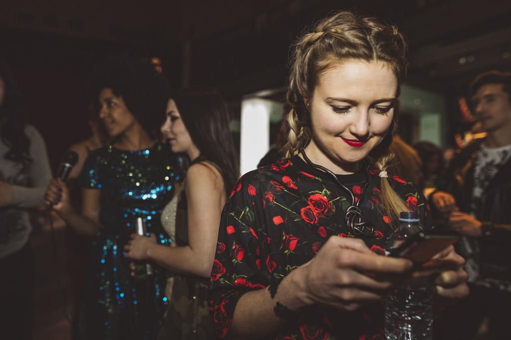 Smiling female millennial texting with smart phone in nightclub