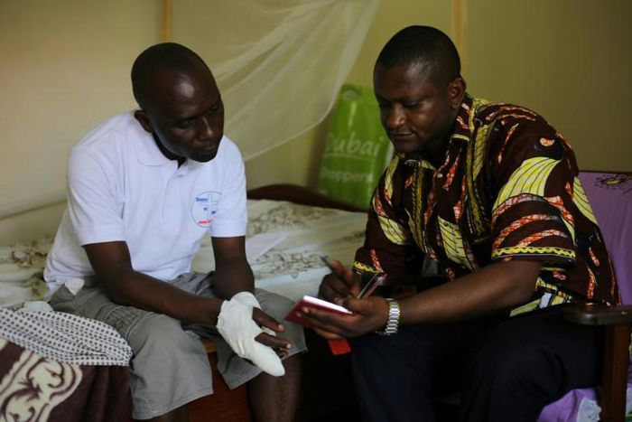 Father Guy-Robert Mandro, shown with a visitor to his home as he recovers from his maiming