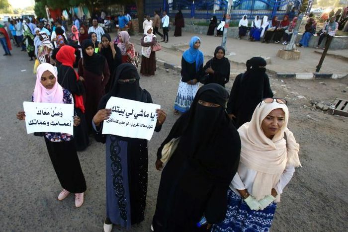 Sudanese protesters hold signs that read: "Take your uncles and aunts with you" and "You who's going home, give a lift to a couple of people"
