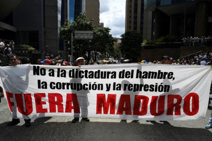 Supporters of Venezuelan opposition leader Juan Guaido hold a banner reading "Maduro Out" as they protest against President Nicolas Maduro in Caracas