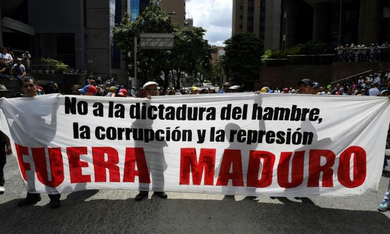 Supporters of Venezuelan opposition leader Juan Guaido hold a banner reading "Maduro Out" as they protest against President Nicolas Maduro in Caracas