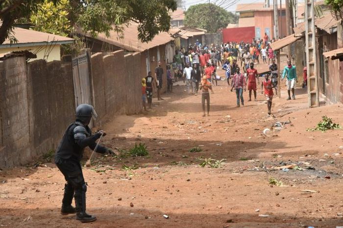 An anti-riot policeman faces young demonstrators in Conakry -- one of many protests that have unfurled over planned changes to the constitution